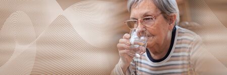 Elderly woman drinking water at home; panoramic bannerの写真素材