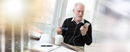 Senior businessman using earphones during conversation on mobile phone; multiple exposure