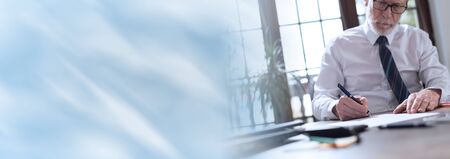 Businessman signing a document in office; panoramic banner