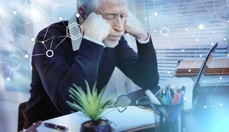 Portrait of overworked senior businessman sitting in office; light effect