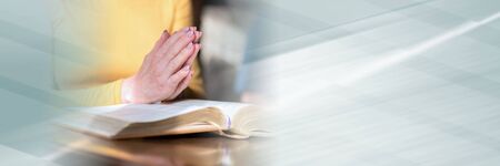 Close up of woman praying with her hands over the bible; panoramic banner