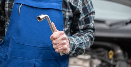 Car mechanic holding tools with car engine on backgroundの写真素材