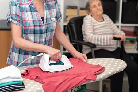 Home helper ironing clothes for elderly womanの写真素材