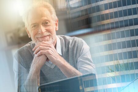 Portrait of smiling senior businessman sitting in office; multiple exposure