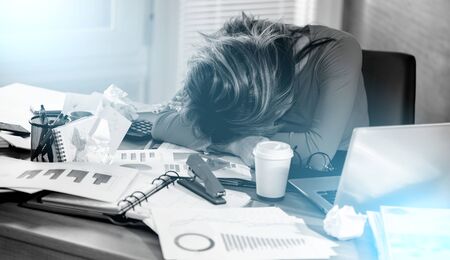 Overworked and exhausted businesswoman sitting at a messy desk; light effect