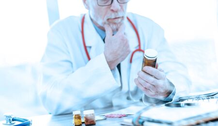 Doctor looking at a bottle of pills in medical office; light effectの写真素材