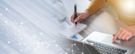 Businesswoman taking notes while using laptop; panoramic banner