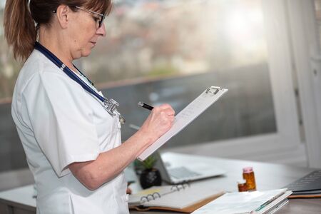 Female doctor taking notes on clipboard in medical officeの写真素材