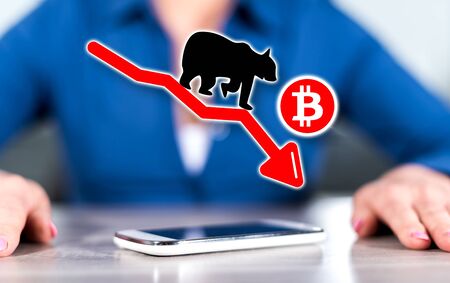 Smartphone with bitcoin bearish trend concept between hands of a woman in backgroundの写真素材