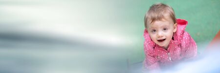 Cute baby girl having fun on a playground and looking the camera; panoramic bannerの写真素材