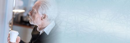 Thoughtful senior man holding a paper coffee cup; panoramic bannerの写真素材