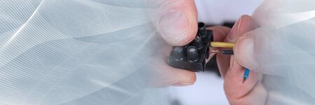 Hand putting a wire in a connector; panoramic banner