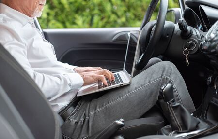 Businessman sitting in car and using his laptop