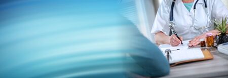 Female doctor writing prescription to her patient in medical office; panoramic bannerの写真素材