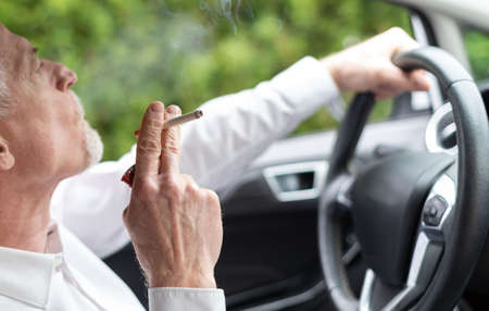 Senior man smoking a cigarette while driving