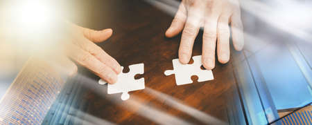 Hands joining two puzzle pieces, teamwork concept; multiple exposure