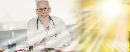 Portrait of male senior doctor sitting in medical office; multiple exposureの写真素材