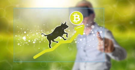 Man with vr headset touching a bitcoin bullish trend concept on a touch screen with his fingerの写真素材