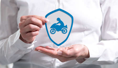 Concept of motorbike insurance with paper shield held by female handの写真素材