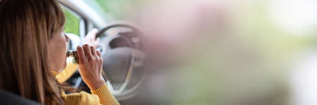 Woman smoking an e-cigarette while driving; panoramic banner
