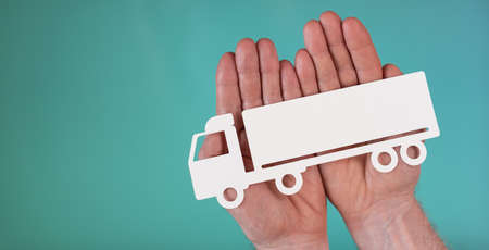 Concept of truck insurance with paper truck in hands on turquoise color backgroundの写真素材