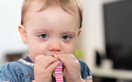Cute baby girl biting a plastic clip and looking at the camera