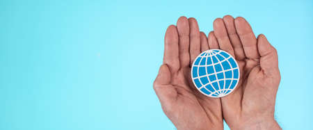 Hands holding a paper earth on light blue background; Concept of planet protectionの写真素材