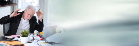 Overworked senior businessman sitting at a messy desk; panoramic bannerの写真素材