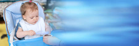 Cute baby girl eating tasty food and learning using spoon; panoramic banner