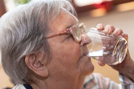 Elderly woman drinking water at homeの写真素材