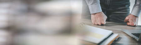 Enraged businessman banging his clenched fists on the desk; panoramic bannerの写真素材