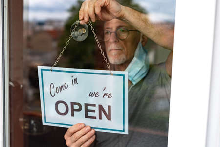 Store owner hanging come in we're open sign on window