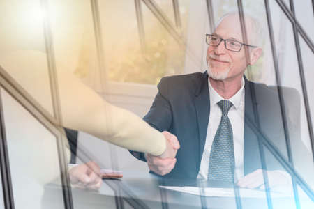 Smiling adviser shaking hand with client after signing a contract, light effect; multiple exposure