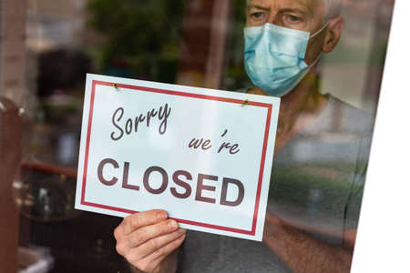 Store owner holding sorry we're closed sign behind the windowの写真素材