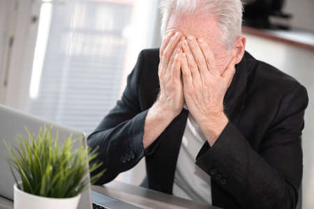 Overworked and exhausted senior businessman sitting at workplace