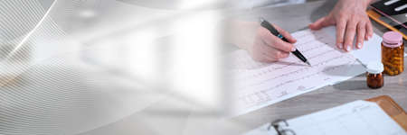 Female cardiologist examining an ecg graph in medical office; panoramic bannerの写真素材