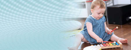 Baby girl sitting on the floor and playing on a xylophone; panoramic bannerの写真素材