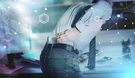 Businessman suffering from back pain in office, light effect