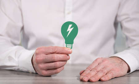 Man holding a green paper light bulb; Concept of clean energy