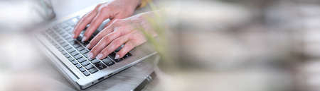 Female hands working on laptop in office; panoramic banner