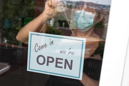 Woman wearing medical face mask hanging come in we're open sign on windowの写真素材