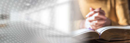 Close up of woman praying with her hands over the bible, hard light; panoramic banner