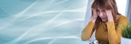Exhausted businesswoman sitting in office with hands on forehead; panoramic banner