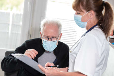 Female doctor discussing with senior man patient in protective medical mask; medical consultation...