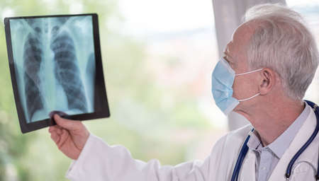 Doctor wearing a medical face mask and examining lungs x-ray during coronavirus outbreak
