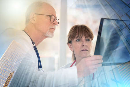 Two doctors examining x-ray report in medical office; multiple exposure