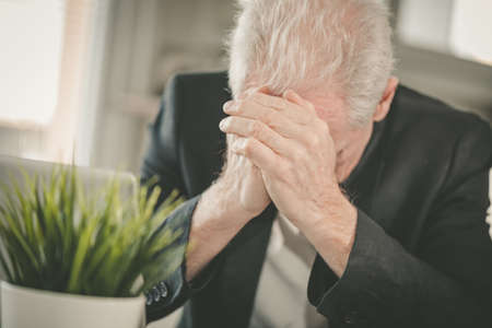 Overworked and exhausted senior businessman sitting at workplace