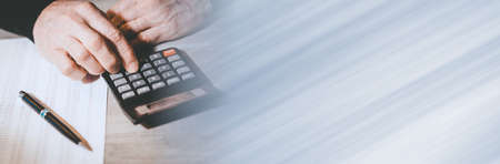 Male hand using a calculator, closeup; panoramic banner