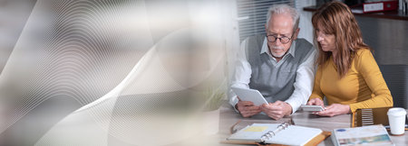 Two mature coworkers working on digital tablet at office; panoramic banner