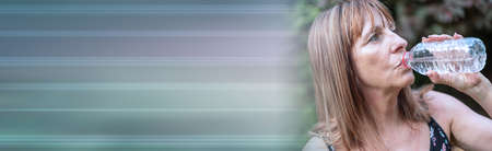 Mature woman drinking water from bottle; panoramic bannerの写真素材